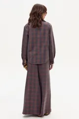 Camisa de lino con estampado escocés en tonos tierra, azul y rojo. Posee cuello con detalle de piel color púrpura y cierre frontal de botones.