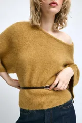 Jersey de punto color mostaza con cuello redondo y mangas amplias tipo murciélago. Presenta un diseño ajustado en la cintura con un cinturón fino de cuero sintético en color marrón a contraste.