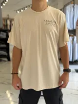 Remera oversize color beige, con diseño estampado en la espalda que incluye tipografía grande y texto descriptivo en negro.