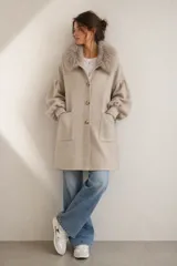 Sacón de lana merino color beige, con cuello de piel sintética, cierre frontal con botones, mangas abullonadas con puños elásticos y bolsillos frontales.