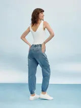 Pantalón jean de corte relaxed, con diseño cargo, cintura elástica con cordón ajustable y puños elastizados en los tobillos. Presenta bolsillos laterales en las piernas y bolsillos traseros.