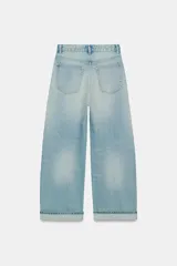 Jeans de tiro medio con cinco bolsillos, trabillas y cierre frontal con cremallera y botón metálico. Presenta un diseño baggy con piernas anchas, roturas decorativas y dobladillo vuelto en los bajos.
