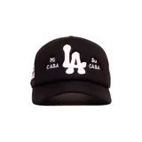 Gorro trucker negro con diseño frontal bordado en color blanco que incluye el logotipo 'LA' y las frases 'Mi CASA' y 'Su CASA'. Cuenta con visera curva y paneles laterales y traseros de red.