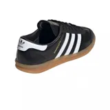 Championes adidas modelo Hamburg, de diseño clásico con exterior de cuero negro, las icónicas tres tiras laterales en blanco y suela de goma color caramelo. Incluye el nombre del modelo en letras doradas en el lateral.