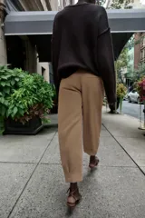 Pantalón de tiro medio con pinzas delanteras, bolsillos laterales y falsos bolsillos de vivo en la parte trasera. Presenta un corte holgado que se estrecha hacia el tobillo, con bajo acabado en pliegues y cierre frontal con cremallera, botón interior y gancho.