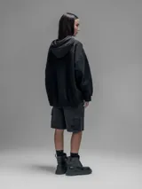Hoodie oversize color negro, confeccionado en frisa gamuzada de algodón con recortes en hombros y bolsillo frontal tipo cargo con solapa en material técnico. Presenta capucha forrada y puños y ruedo acanalados.