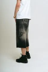 Bermuda de jean estilo carpintero, corte baggy, color negro lavado con efecto degradado. Presenta bordados en la parte trasera con tipografía gótica que dice "Lucca Bossio". Incluye bolsillos grandes y bolsillo lateral de carpintero.