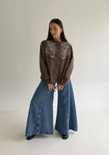 Camisa color marrón chocolate con bordado artesanal de flores y hojas en hilo crudo. Presenta cuello con volado, mangas largas con puños abotonados y cierre frontal con botones.