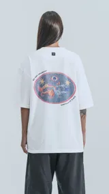 Remera blanca de corte oversize con estampa circular en la espalda que presenta un diseño artístico de dragones, estrellas y un ojo central con la leyenda No Art Uruguay y Castillo de Piria.