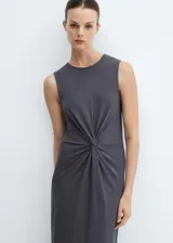 Vestido midi sin mangas de algodón, con cuello redondo y diseño recto. Presenta un detalle de nudo central que genera un efecto drapeado en la parte frontal.