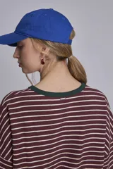 Remera oversize a rayas horizontales en tonos bordó y blanco, con cuello redondo verde oscuro y un pequeño parche bordado en forma de corazón en el pecho.