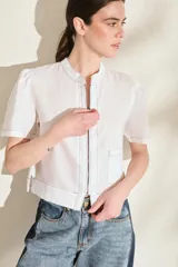 Blusa de lino color amarillo, con cuello mao, cierre frontal con cremallera y mangas cortas abullonadas. Cuenta con un bolsillo aplicado en el frente.