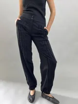 Pantalón tipo babucha confeccionado en lana de oveja, color visón. Presenta un diseño de tiro alto con textura vertical plisada a lo largo de las piernas, cintura con cierre de doble broche y puños elásticos en los tobillos.