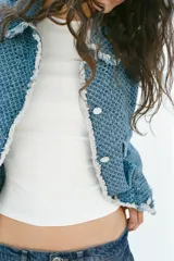 Chaqueta de denim de corte clásico con textura perforada, cuello solapa, bolsillos delanteros de plastrón, cierre frontal con botones a contraste y detalles de flecos en los bordes.