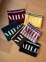 Clutch de neopreno color marrón oscuro con cierre de cremallera metálica dorada. Presenta la inscripción "MILO" en letras blancas de gran tamaño en el frente.
