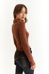 Top de manga larga color verde petróleo, con cuello polo y escote en V pronunciado. Presenta recortes diagonales en el frente y un pequeño bordado en el puño.