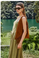 Bolso tipo hobo de gamuza color marrón, con diseño de flecos en los laterales y correa integrada al cuerpo del bolso.