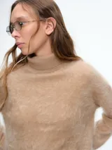 Sweater de cuello alto con textura peluda, confeccionado en tejido de punto suave y holgado, con mangas largas y puños ajustados.