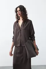 Camisa negra de corte relajado y caída fluida, con cuello clásico, escote en V y cierre frontal con botones forrados. Presenta mangas largas con puños abotonados.