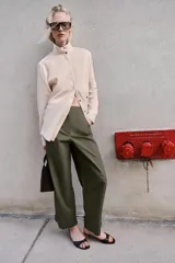Pantalón de tiro alto en color verde militar, con corte barrel de pernera holgada que se estrecha hacia el tobillo. Presenta trabillas laterales ajustables en la cintura y en el bajo, bolsillos delanteros y cierre frontal con cremallera y botón.