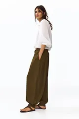 Pantalón globo verde militar de corte holgado en tejido con leve brillo, con elástico fruncido y cordón ajustable en la cintura, bolsillos laterales y puños abotonados en el bajo.