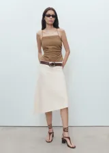 Falda midi evasé de tiro medio, confeccionada en mezcla de algodón y lino, con diseño asimétrico en el bajo y cierre de cremallera lateral.