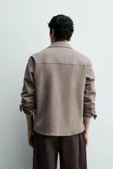 Sobrecamisa de corte regular fit en tejido elástico y transpirable, con cuello solapa, cierre frontal mediante botones a presión y bolsillo de plastrón en el pecho. Presenta mangas largas con puños abotonados y bajo con aberturas laterales.