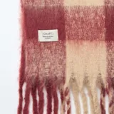 Bufanda de tejido suave con diseño de cuadros grandes en tonos rojo y beige, terminada con flecos en los extremos.