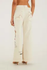 Pantalón de tiro alto y pierna ancha, confeccionado en denim color crudo con costuras a la vista en tono óxido. Presenta un diseño estampado de sellos vintage, flores y postales.
