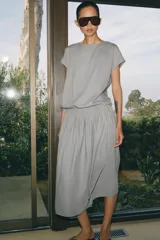 Vestido midi de Zara Woman Collection confeccionado en hilatura con lino, color gris. Presenta cuello redondo, manga corta caída, detalle de frunces y lazadas laterales en el mismo tejido, y cierre en la espalda.