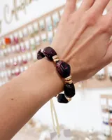 Pulsera elástica compuesta por piedras irregulares de color bordó veteado intercaladas con cuentas metálicas doradas.