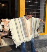 Poncho de lana merino tejido en telar, de diseño amplio con franjas verticales en tonos crudo, beige, marrón y celeste, y flecos en los bordes.