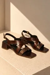 Sandalias de cuero vacuno color beige, con diseño de tiras cruzadas en el empeine, puntera cuadrada, taco bloque mediano y tira ajustable con hebilla en el talón.
