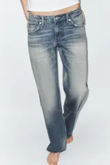 Jeans de tiro bajo y cinco bolsillos, con diseño de pierna ancha y larga. Presenta roturas y desgastes sutiles en la parte delantera. Cierre frontal con cremallera y botón metálico.