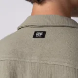 Camisa de manga corta color verde militar, confeccionada en lino entramado, con cuello cubano y cierre frontal con botones.