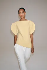 Top amarillo de manga corta abullonada, con cuello barco y bajo asimétrico. Cierre trasero con cremallera oculta.