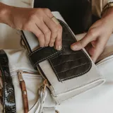 Billetera de cuero color blanco y negro con textura tipo cocodrilo. Tiene bolsillo frontal con solapa, dos bolsillos con cierre en los extremos y dos bolsillos para tarjetas en el interior.