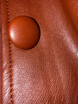 Tapado de cuero sintético color bordó, con cuello y puños de piel sintética desmontables. Presenta cierre frontal con botones y cinturón ajustable con hebilla forrada en el mismo material.