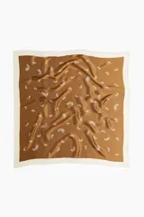 Pañuelo cuadrado de tejido suave y satinado, color marrón camel, con borde liso color crema. Presenta un estampado repetitivo de cachemir (paisley) en color blanco.