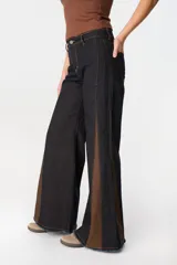 Pantalón de jean de pierna ancha con cortes laterales y paneles triangulares en contraste de color marrón. Presenta costuras a la vista en tono ocre y ruedo desflecado.