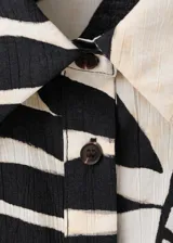 Camisa de manga corta con estampado de hojas en blanco y negro, cuello camisero y cierre delantero con botones.