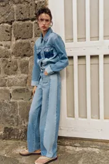 Jeans de tiro medio con diseño barrel y paneles laterales en un tono de denim más claro que contrasta con el centro. Presenta cinco bolsillos, cierre frontal con cremallera y botón, y bajo con acabado sin costura.