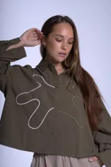 Camisa color verde militar de manga larga con cuello clásico, cierre frontal con botones y bordados abstractos en blanco y verde.