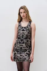 Vestido mini negro sin mangas y cuello redondo, completamente bordado con mostacillas, piedras y lentejuelas en tonos dorados y rosados. Presenta un corte recto con calados que acompañan el diseño.