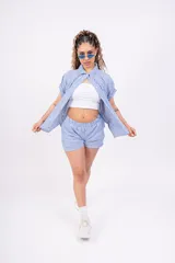 Conjunto de camisa y shorts a rayas verticales celestes y blancas. La camisa es de manga corta y se usa abierta sobre un top blanco.