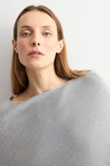 Capa tejida en hilo de lurex color beige, con cuello bote y diseño asimétrico de corte fluido.