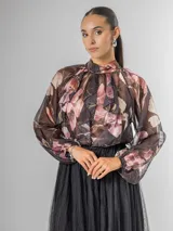 Camisa de seda italiana con estampa floral en tonos rosados y marrones sobre fondo oscuro. Presenta cuello alto con volados y lazo para atar en la espalda, y mangas abullonadas.