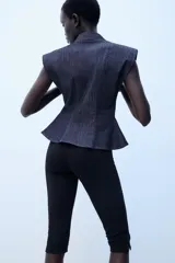 Camisa sin mangas de denim azul oscuro, con cuello solapa, hombreras marcadas, bolsillos delanteros de plastrón, bajo con peplum y cierre frontal con botones metálicos.