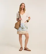 Vestido corto de corte recto y escote en V, color beige claro con estampado de paisaje tropical con palmeras en la parte inferior, mangas cortas y bolsillos laterales. Marca Marfinno.