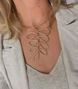 Gargantilla rígida dorada con dije colgante en forma de hoja estilizada.